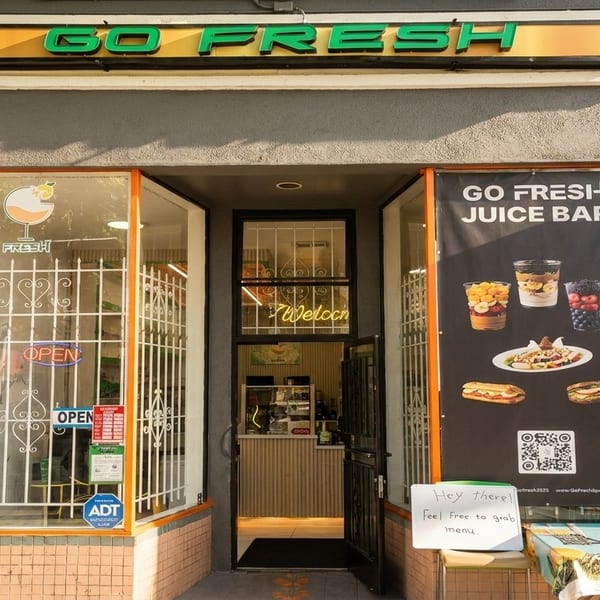 The storefront of Go Fresh Juice Bar, with an open door and a menu board displaying juices and sandwiches.